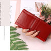 A red genuine leather wallet is shown open, resting on a light pink background next to floral arrangements and green foliage.