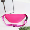 A bright pink multi-layer sports waist bag is displayed on a white surface next to a framed feather and a green palm leaf.