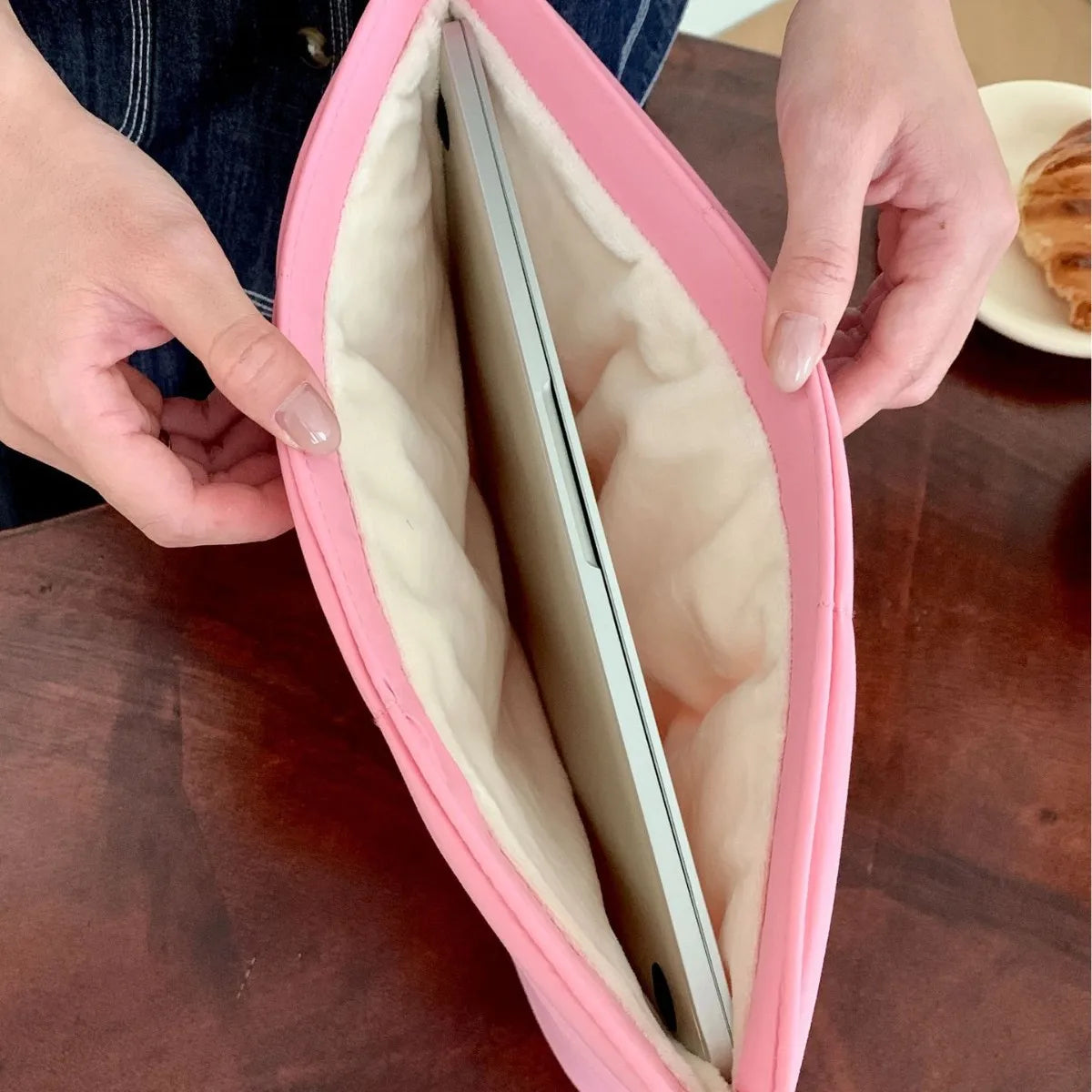 A person holds a pink quilted laptop sleeve open, revealing a silver laptop inside.