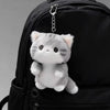 A grey soft cat plush pendant ornament attached to a black backpack.