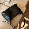 A black retro PU leather underarm bag resting on a light beige surface with small white cups.