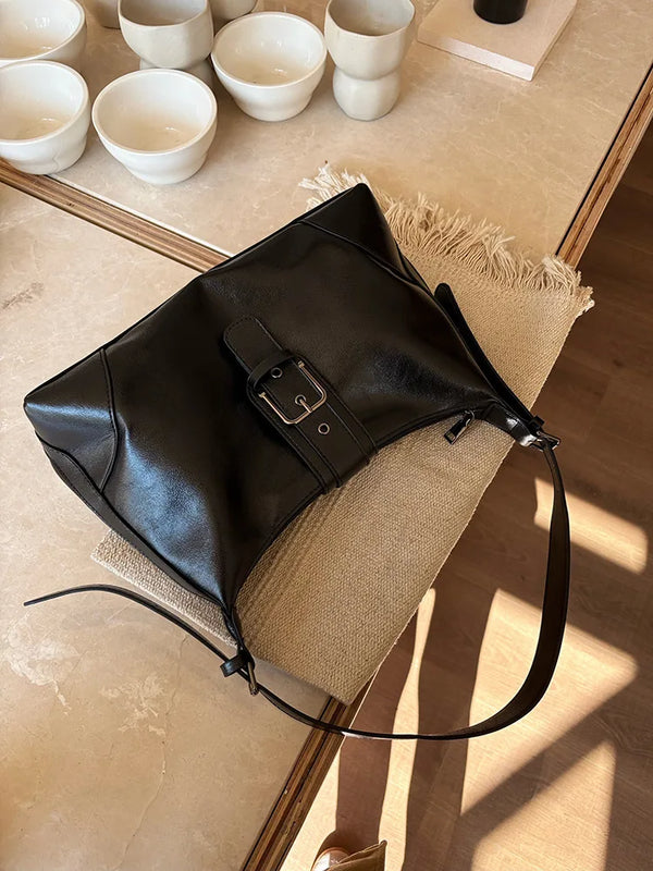 A black retro PU leather underarm bag resting on a light beige surface with small white cups.
