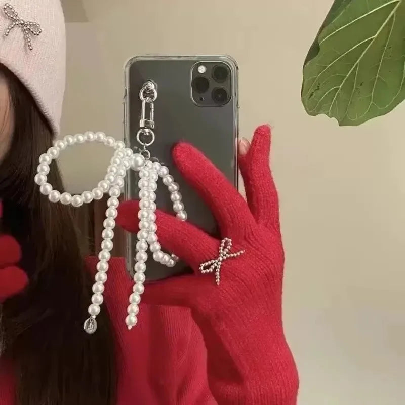 A hand wearing a red sweater holds a smartphone displaying a pearl and bowknot keychain.