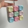 A hand holds a clear plastic container filled with colorful, square tactile stress relief keyboard fidget toys.