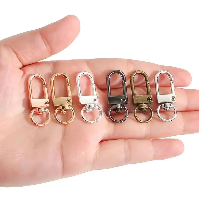 Eine Hand hält mehrere Metall-Scharnierhaken für Taschen und Gürtel in verschiedenen Größen und Oberflächen.
