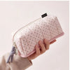 A pink pencil case with a dot pattern is held by a hand against a light background.