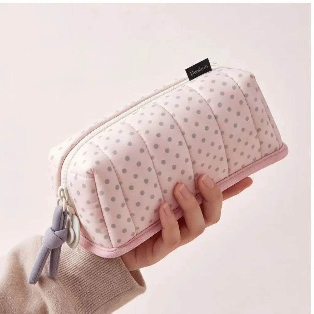 A pink pencil case with a dot pattern is held by a hand against a light background.