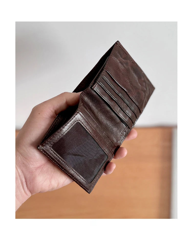 A hand holds a dark brown genuine leather bifold wallet displaying stitched lines and a suede flap.