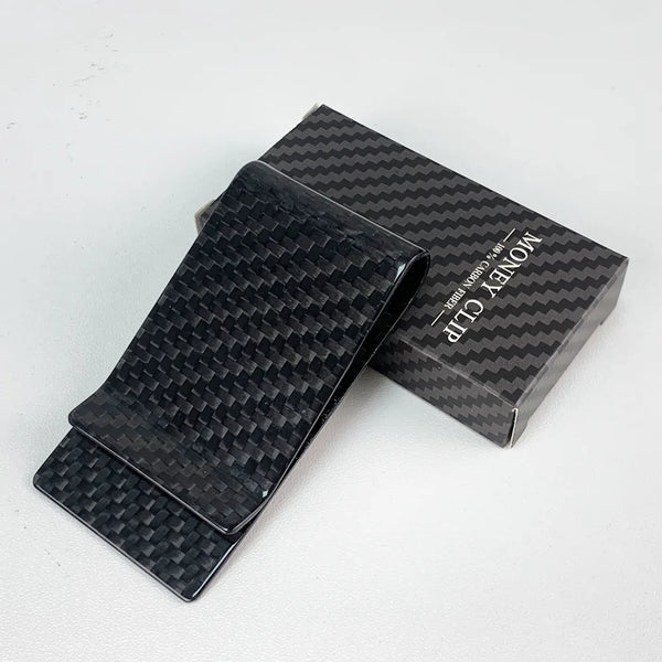 A black carbon fiber money clip is displayed next to its original packaging.