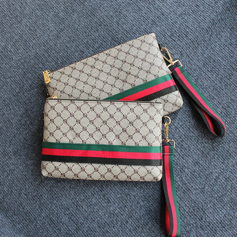 Beige und grün gemusterte Clutch-Tasche mit schwarzem Zierrand auf blauem Stoffhintergrund.