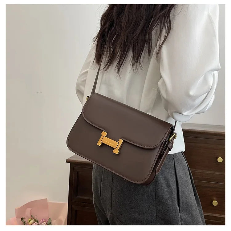 Eine braune Leder-Ein-Schultertasche, getragen von einer Person in weißem Hemd und grauem Rock.