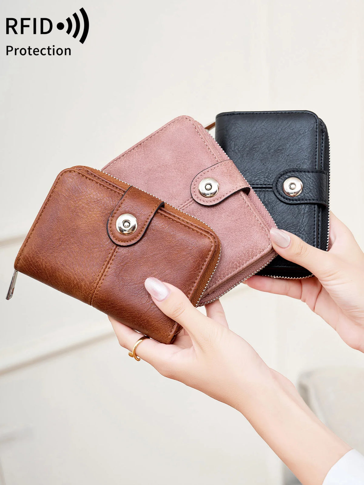 A hand holds a brown leather wallet and a pink leather wallet, demonstrating RFID protection.