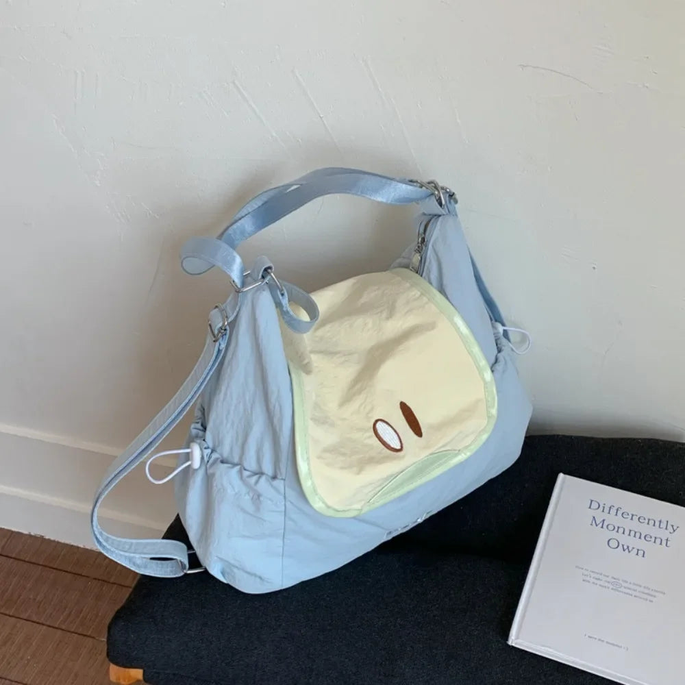 Light blue nylon messenger backpack with a pale yellow patch and brown embroidered eyes