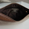 A close-up view of a metallic silver alligator print clutch bag with a gold zipper and interior lining.