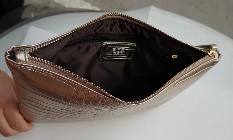 A close-up view of a metallic silver alligator print clutch bag with a gold zipper and interior lining.