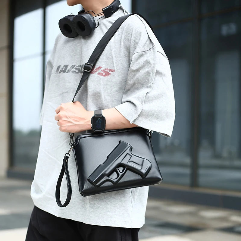 A man wearing a gray t-shirt and black accessories holds a black embossed crossbody clutch bag featuring a pistol design.