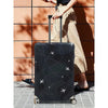 A black suitcase with an airplane pattern protector cover is being pulled by a person.