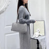 A woman wearing a gray knitted dress holds a black and white checkered nylon shoulder tote bag.