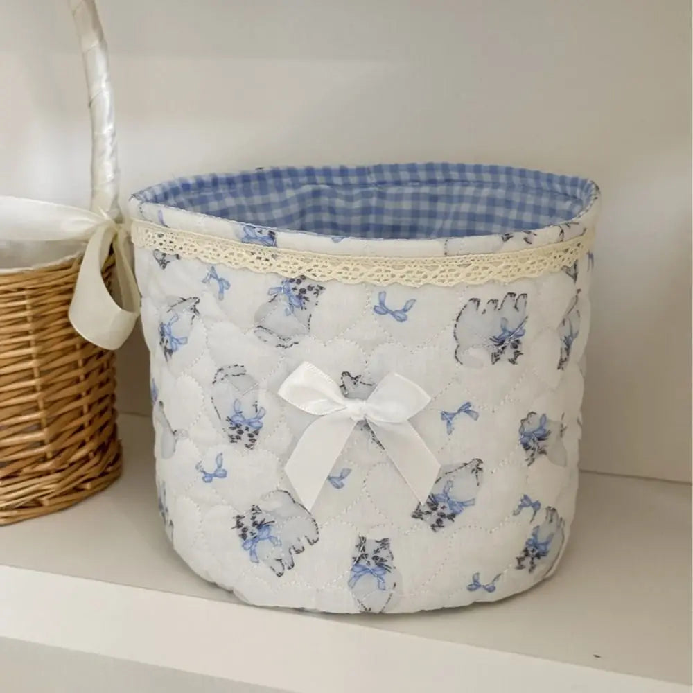 Cesta de almacenamiento de corazón acolchada de algodón blanco con patrones florales azules, junto a una cesta tejida.