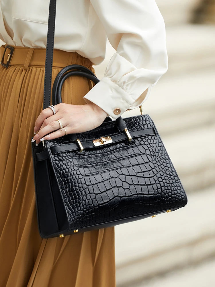 A black genuine leather shoulder bag carried by a person wearing a mustard yellow skirt and white blouse.