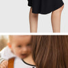 A close-up of a tan leather backpack diaper bag with gold zippers being held by a baby.
