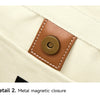 Detail of a brown metal magnetic closure on a cream-colored fabric.