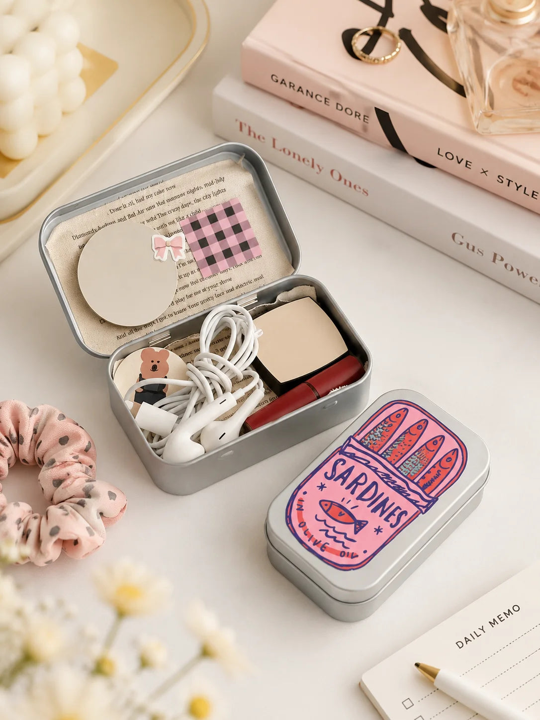 A portable metal storage box with a sardine print design and white accessories is shown on a light surface.