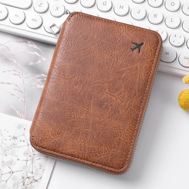 A brown leather passport and document holder with a small airplane embossed on the cover, resting on a white keyboard.