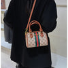 A black top wearing an elegant leather tote diaper bag with a green and red striped pattern and a brown crossbody strap.