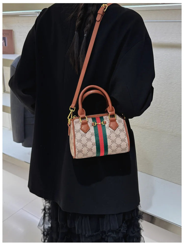 A black top wearing an elegant leather tote diaper bag with a green and red striped pattern and a brown crossbody strap.