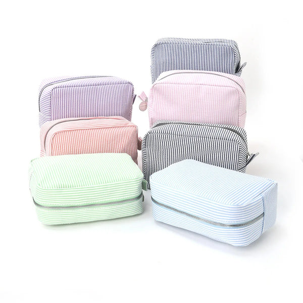 A collection of five striped cosmetic bags in shades of pink, purple, and green stacked on a white background.