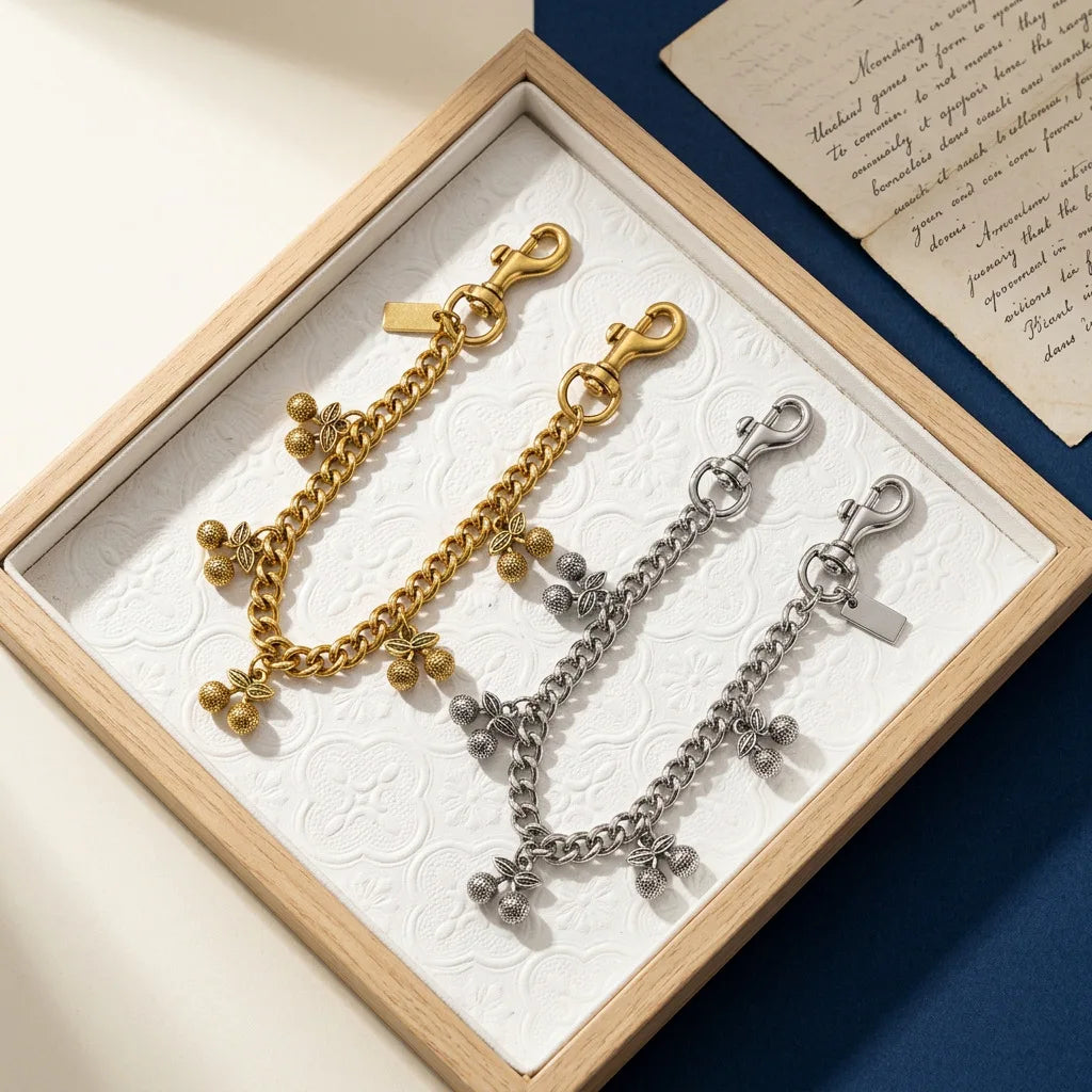 Un juego de llaveros con charms de cadena de cereza dorados y plateados, exhibidos en una caja de madera.