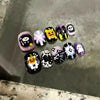 A collection of colorful press-on nails featuring skull and cartoon designs displayed on a gray surface.