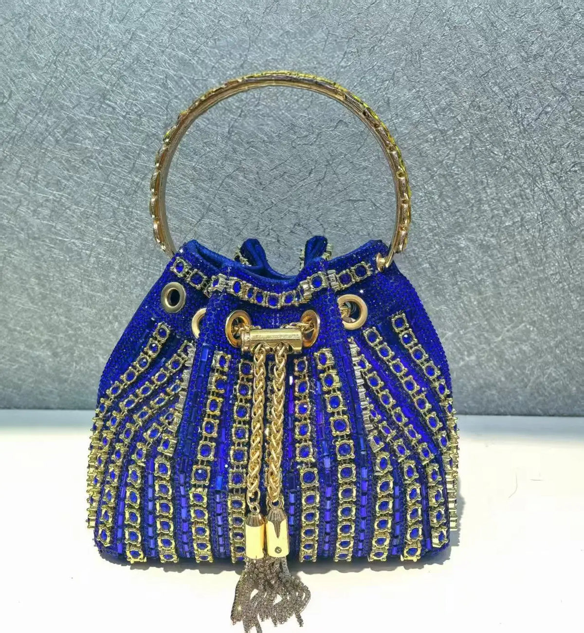 A royal blue crystal-embellished evening clutch with a gold chain handle and tassel.