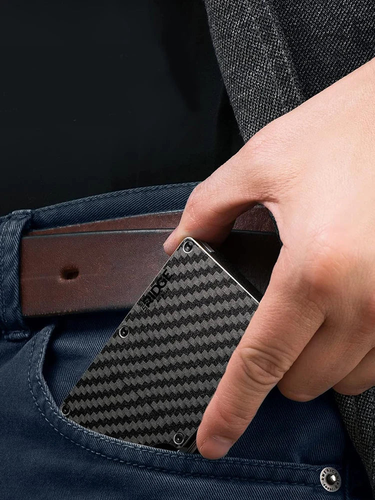 A hand is inserting a black patterned slim RFID blocking wallet into the pocket of dark blue fabric.