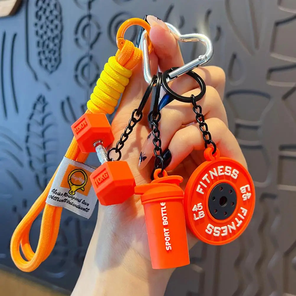 An orange fitness keychain featuring a dumbbell and kettlebell charm attached to a metal ring.