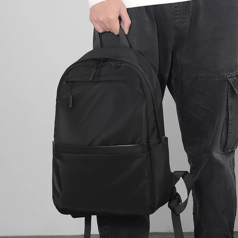 A man is holding a black lightweight laptop backpack with large capacity.