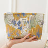 A hand holds a floral canvas makeup bag featuring blue and yellow flowers and green leaves.