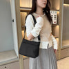 A woman holds a black waterproof nylon crossbody bag in a light beige sweater and gray pleated skirt.