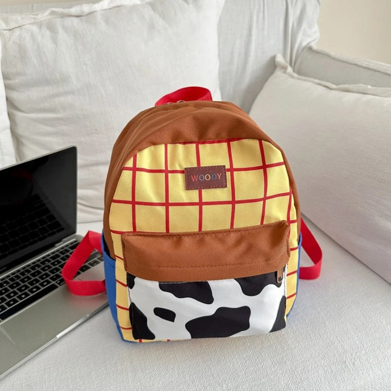 A brown and yellow plaid backpack with a cow print front is resting on a white surface next to a laptop.