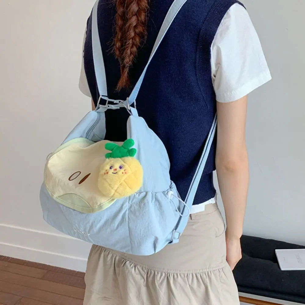 A person wearing a navy blue vest and light shirt carries a light blue nylon messenger backpack with a yellow lemon charm.