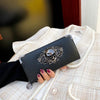 A black leather wallet with an ornate skull design is held in a hand against a light plaid jacket.