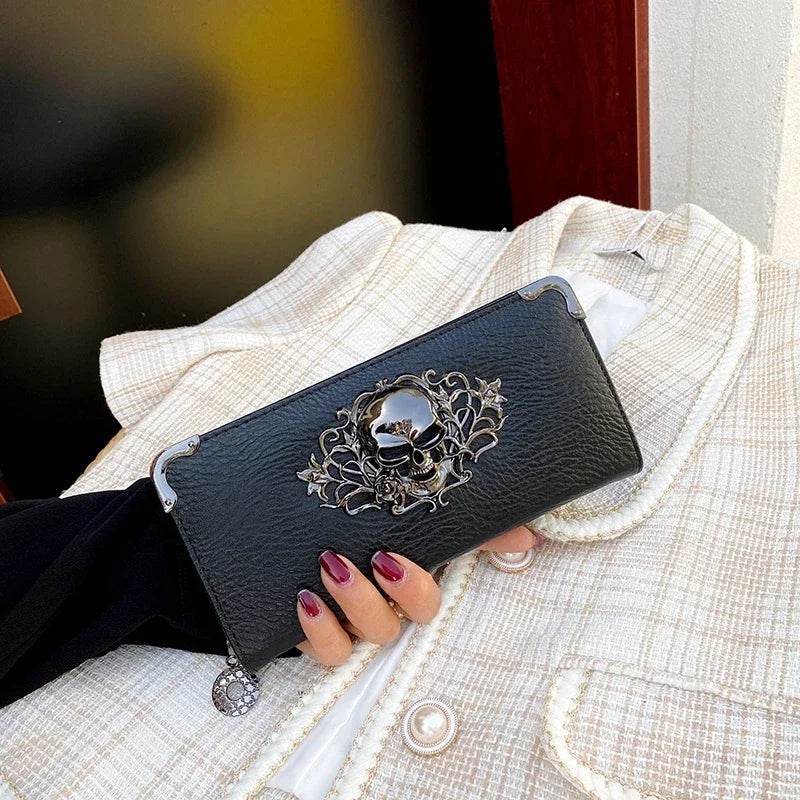 A black leather wallet with an ornate skull design is held in a hand against a light plaid jacket.