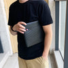 A person holding a black PU leather clutch bag in front of a light-colored wall.