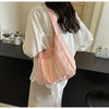 A woman holds a striped canvas shoulder bag with a magnetic closure against a white shirt.