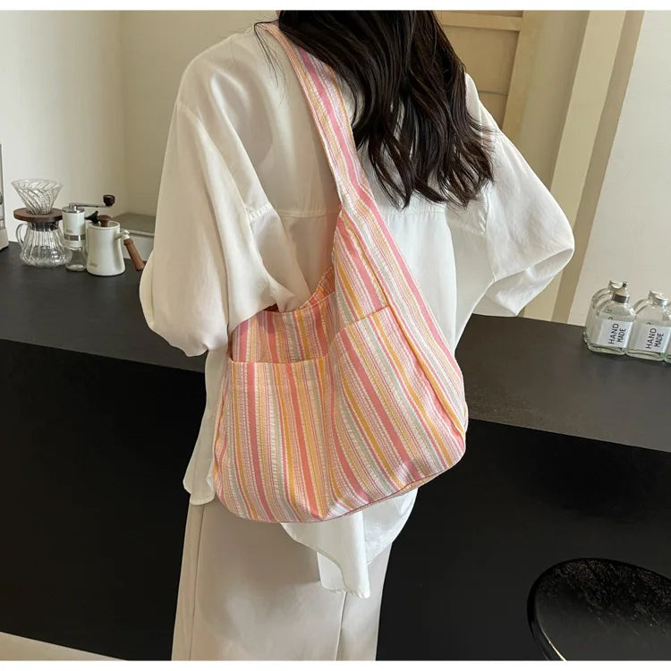 A woman holds a striped canvas shoulder bag with a magnetic closure against a white shirt.