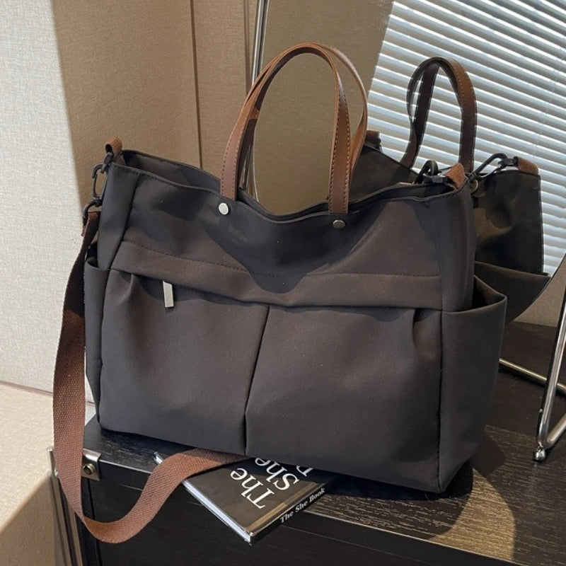 A dark gray lightweight nylon tote bag with brown leather handles and multiple internal pockets.