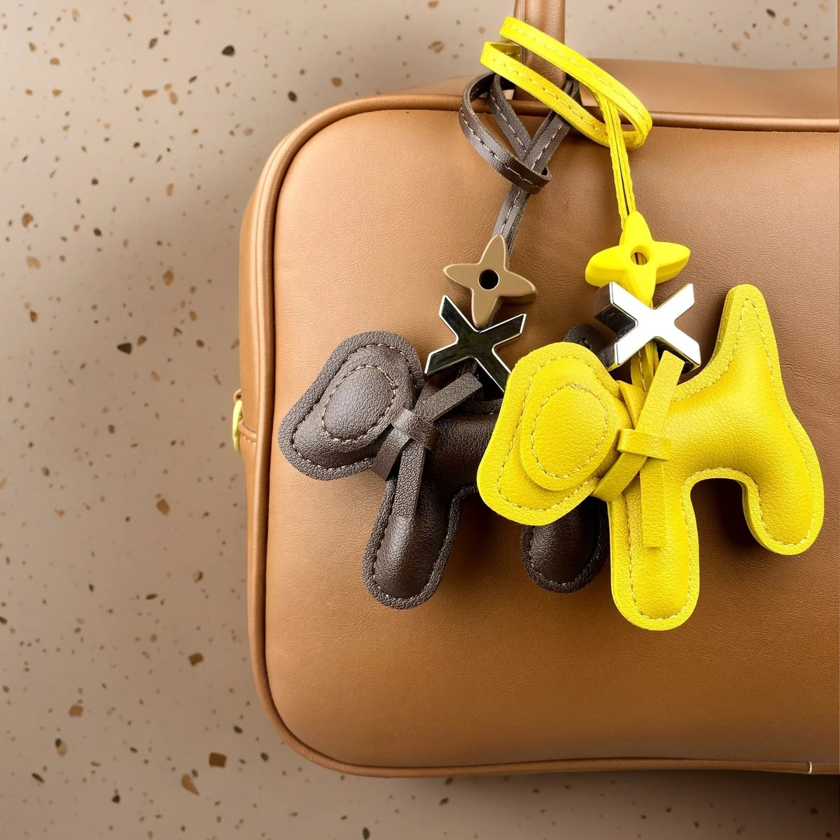 A yellow and brown PU leather puppy bag charm with a bow tie hanging from a tan leather backpack.