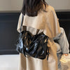 A woman is shown from the back wearing a beige trench coat and carrying a black leather shoulder bag.