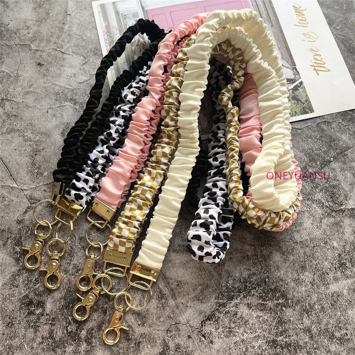 Präsentation eleganter goldener Schlüsselketten und Lanyards in Pastellrosa, Creme und Schwarz